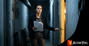 Young actor standing backstage before their first audition, script in hand, looking toward the light of the audition room door with determination