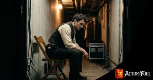 Actor sitting alone backstage in dim light with head bowed, reflecting the emotional weight of performing and actor mental health challenges